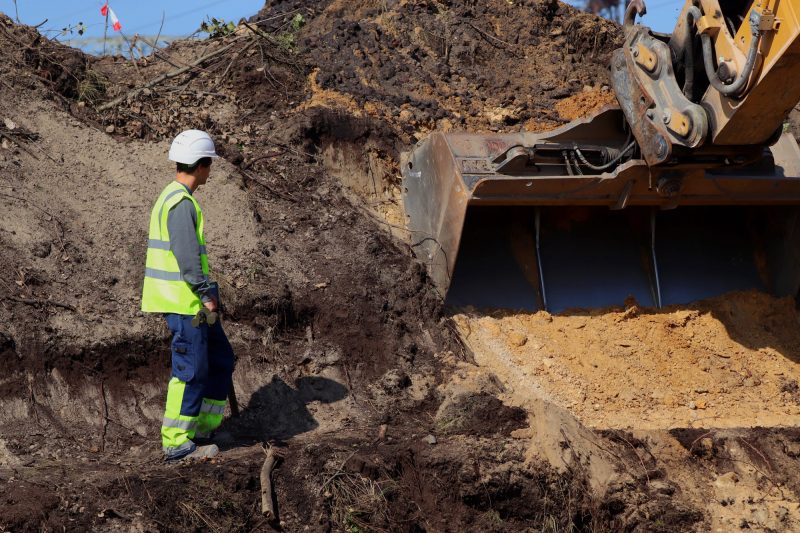 Baubegleitende Erdarbeiten große Baggerschaufel beim Aushub von Erde daneben ein Mitarbeiter