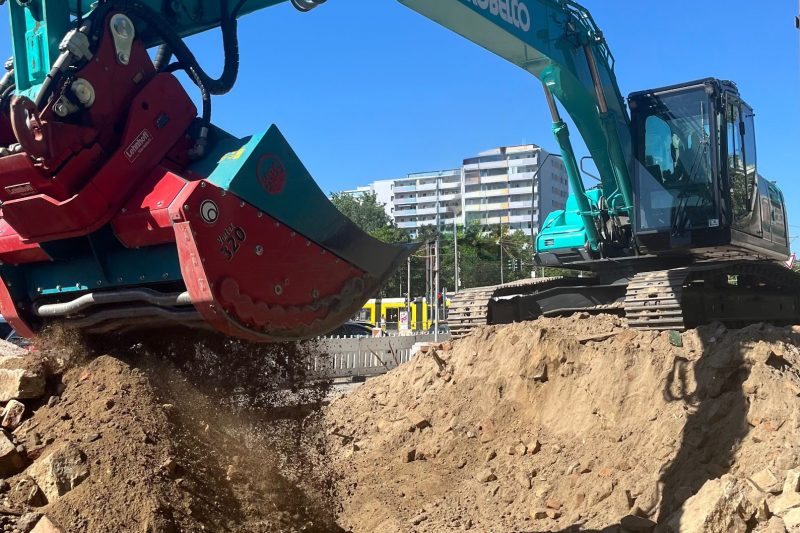 sieben-volumenraeumung-bagger-baumassnahme Sieben von Bodenaushub mit Sieblöffel an einem Bagger während einer Volumenräumung auf einer Baustelle.